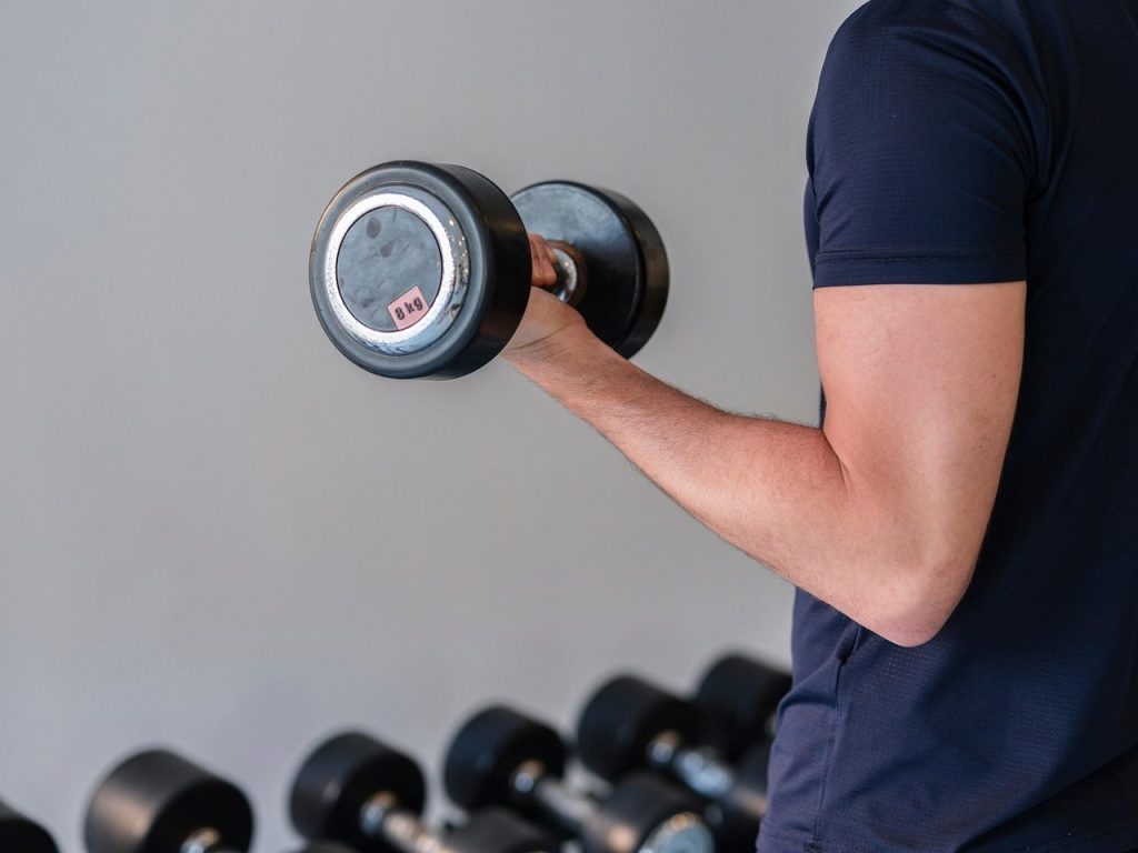 Person in a dark shirt lifting an 8 kg dumbbell in one hand, performing a bicep curl at the gym.